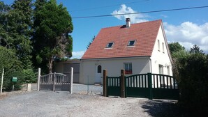 Een huis met twee verdiepingen, een dak van rode tegels, een grindpad en een groene poort.