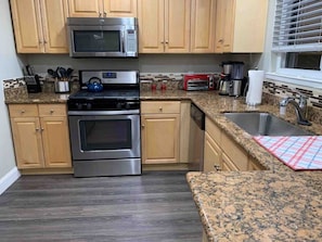 A kitchen with wooden cabinets, a stainless steel microwave, a toaster, and a sink.