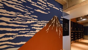 A hallway with a wall mural of a mountain and clouds, wooden flooring, and a clothing rack with hanging items. - Santiago Guesthouse Naha - Hostel (Naha)