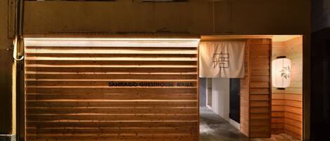 A wooden garage door with the text "SANTIAGO GUESTHOUSE NHA" and a small wooden structure with a lantern.