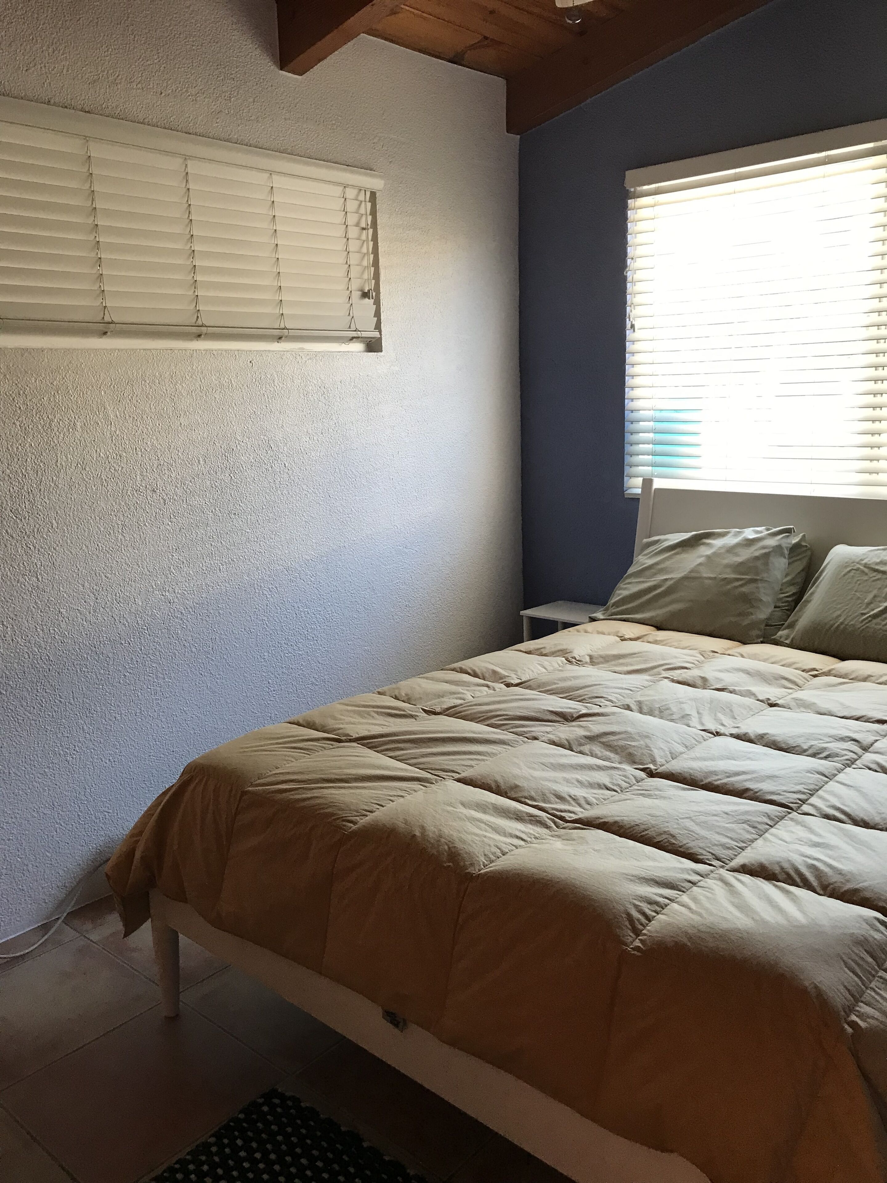A bedroom with a bed, a window with blinds, and a wall with a textured finish.