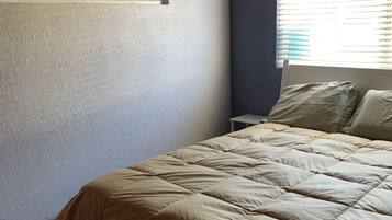 A bedroom with a bed, a window with blinds, and a wall with a textured finish.