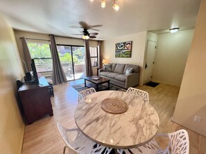 A spacious living area with a round marble table, white chairs, a sofa, and a ceiling fan.