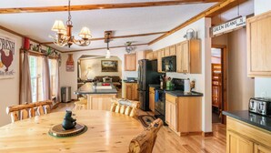 A wooden dining table with chairs, a chandelier, a refrigerator, and wooden cabinets in a kitchen.