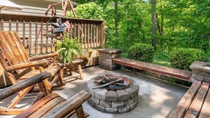 An outdoor patio with a stone fire pit, wooden furniture, and a rustic fence.