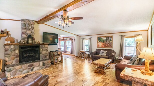 A cozy living room with a stone fireplace, wooden furniture, and a television mounted on the wall.