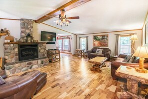 A cozy living room with a stone fireplace, wooden furniture, and a television mounted on the wall. - Hocking Hills Getaway w/ Hot Tub, Sauna & 20 Private Acres. Pet-Friendly! (South Bloomingville)
