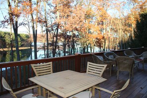 Una terraza de madera con una mesa y sillas, con vistas a un cuerpo de agua y árboles.