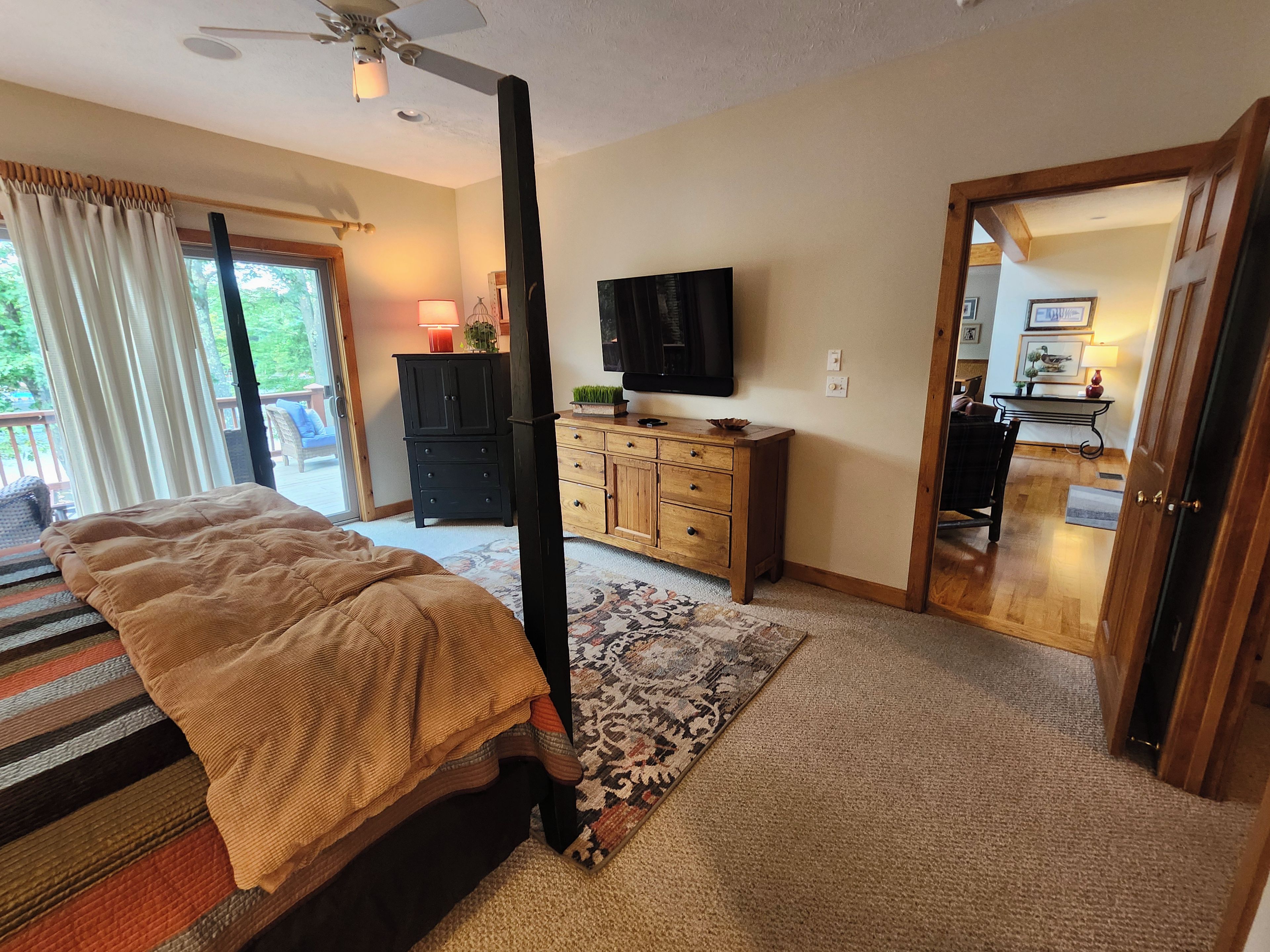 A bedroom with a bed, a television, a dresser, and a door leading to a balcony.