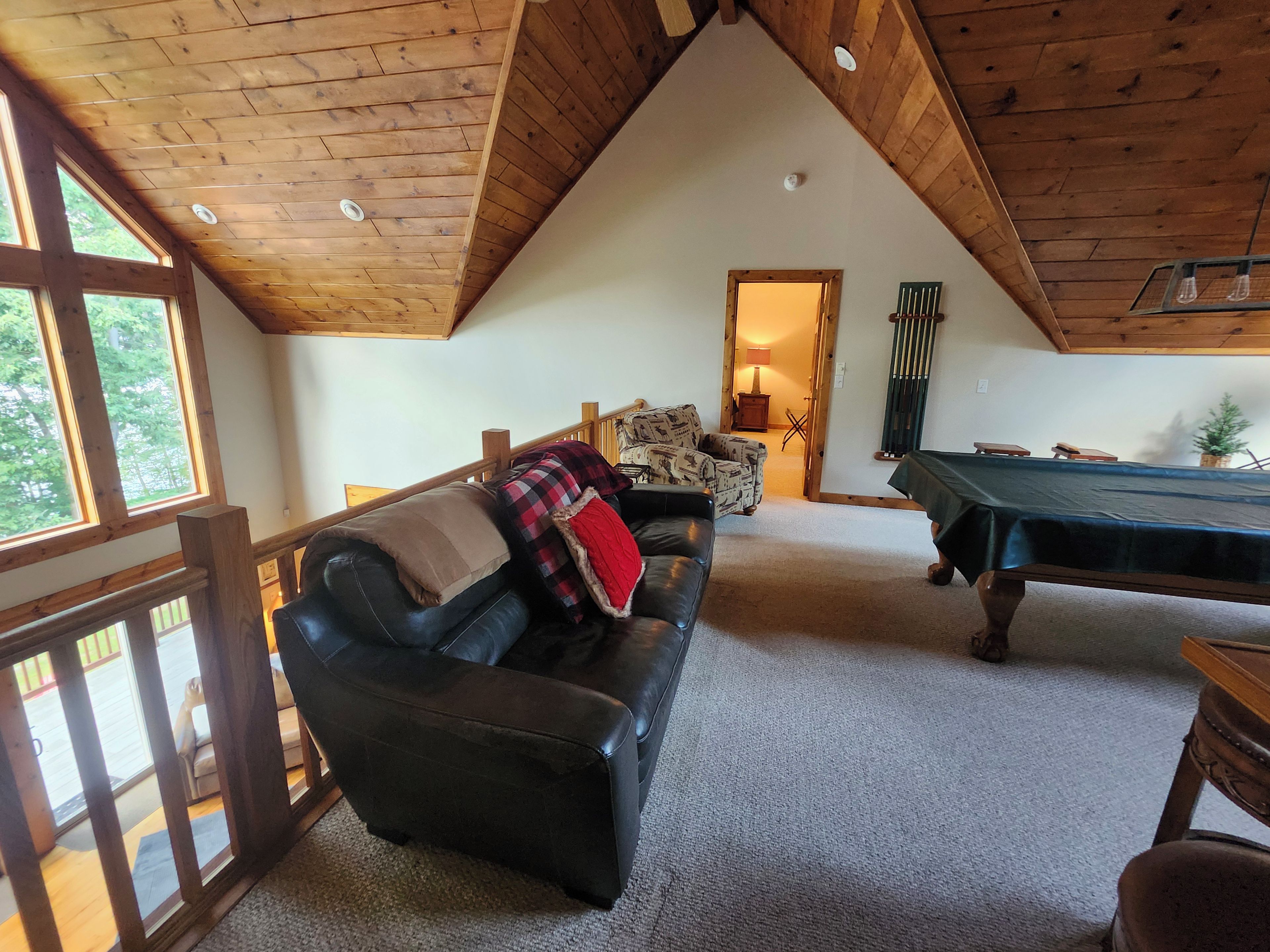Een knus vertrek met houten plafond, een pooltafel, een leren bank en een raam met uitzicht op bomen.