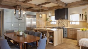 A modern kitchen with wooden beams, a central island, and a dining area with chairs and a table. -  Come Home To Tomorrow's Comforts in Historic CB! Book for summer soon!! (Crested Butte)