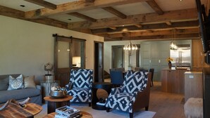A spacious living room with a high ceiling, wooden beams, a sofa, patterned armchairs, a coffee table, and a dining area with chairs and a chandelier. -  Come Home To Tomorrow's Comforts in Historic CB! Book for summer soon!! (Crested Butte)