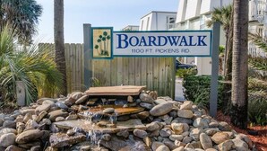 A sign for Boardwalk at 1100 FT. Pickens Rd. with a small waterfall and rocks in the foreground. -  Island's End Welcomes You to Paradise!   (Pensacola Beach)