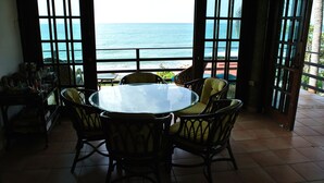 A dining area with a glass table and wicker chairs, overlooking a beach and ocean. - Caribbean Beach Front Gem 2 (Punta Pozuelo, Guyama)