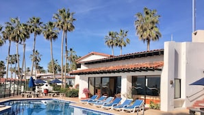 A pool area with lounge chairs, palm trees, and a building with large windows.
