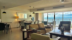 A spacious living area with a dining table, sofas, and a balcony with a view of the ocean.