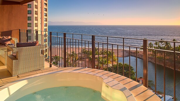 A balcony with a hot tub, overlooking a beach and a body of water.