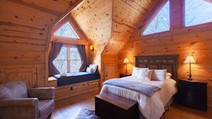 A cozy log cabin bedroom with a large bed, a window seat, and a chair. - 5 Suite Toccoa River Lodge Sleeps 12 | Hot Tub + Game Room | Fishing Access (Blue Ridge)