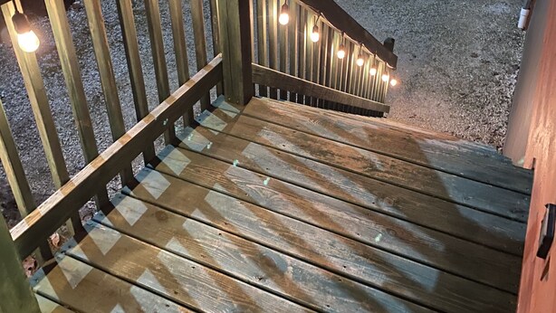 Une terrasse en bois avec une rambarde et des guirlandes lumineuses.