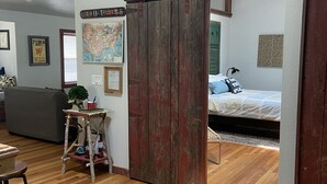 Une pièce avec un plancher en bois, un lit, un bureau, une chaise, une carte accrochée au mur et une porte coulissante.