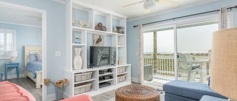 A living room with a TV, shelves, and a view to the outside.