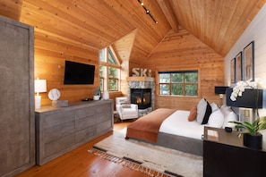 A log cabin bedroom with a fireplace, a bed, a TV, and a stone fireplace surround.