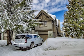 A house with a garage, surrounded by snow-covered trees.