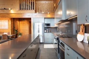 A modern kitchen with stainless steel appliances, a dining area with a wooden table, and a view of the outdoors.