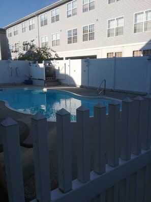 A swimming pool with a wooden fence, a ladder, and a building in the background. - Great Location! Lots of Amenities! (Wildwood)