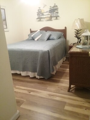 A bedroom with a wooden bed, a nightstand with a lamp, and a wall decoration. - Great Location! Lots of Amenities! (Wildwood)
