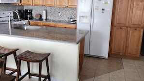 Una cocina con armarios de madera, un refrigerador blanco, un microondas, un lavamanos y un taburete de bar.