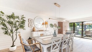 A dining area with a wooden table, white chairs, a large mirror, and a potted plant.