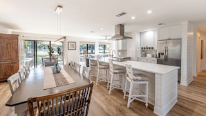 A modern kitchen with white cabinetry, a central island, and a dining area with a wooden table and chairs.