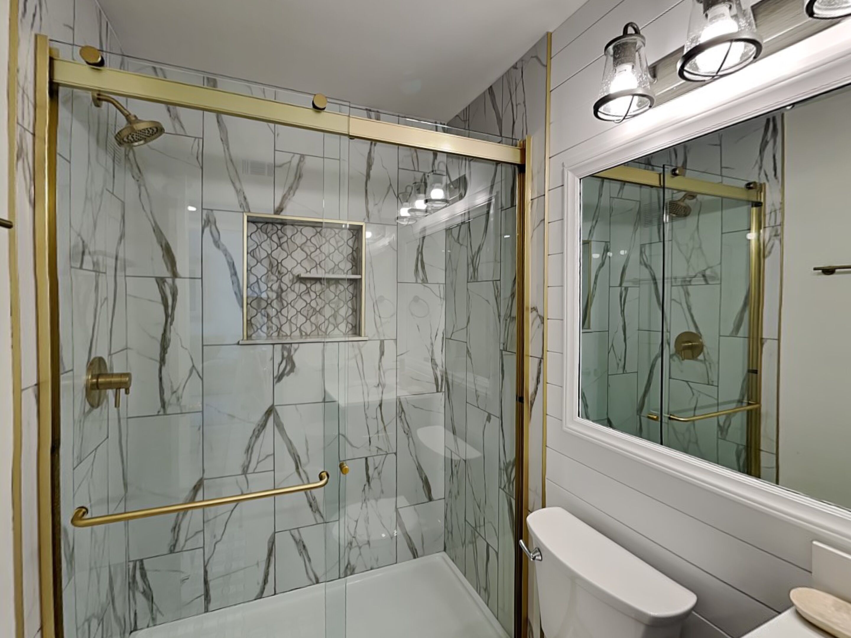 A bathroom with a glass-enclosed shower, a toilet, and a vanity with a mirror.