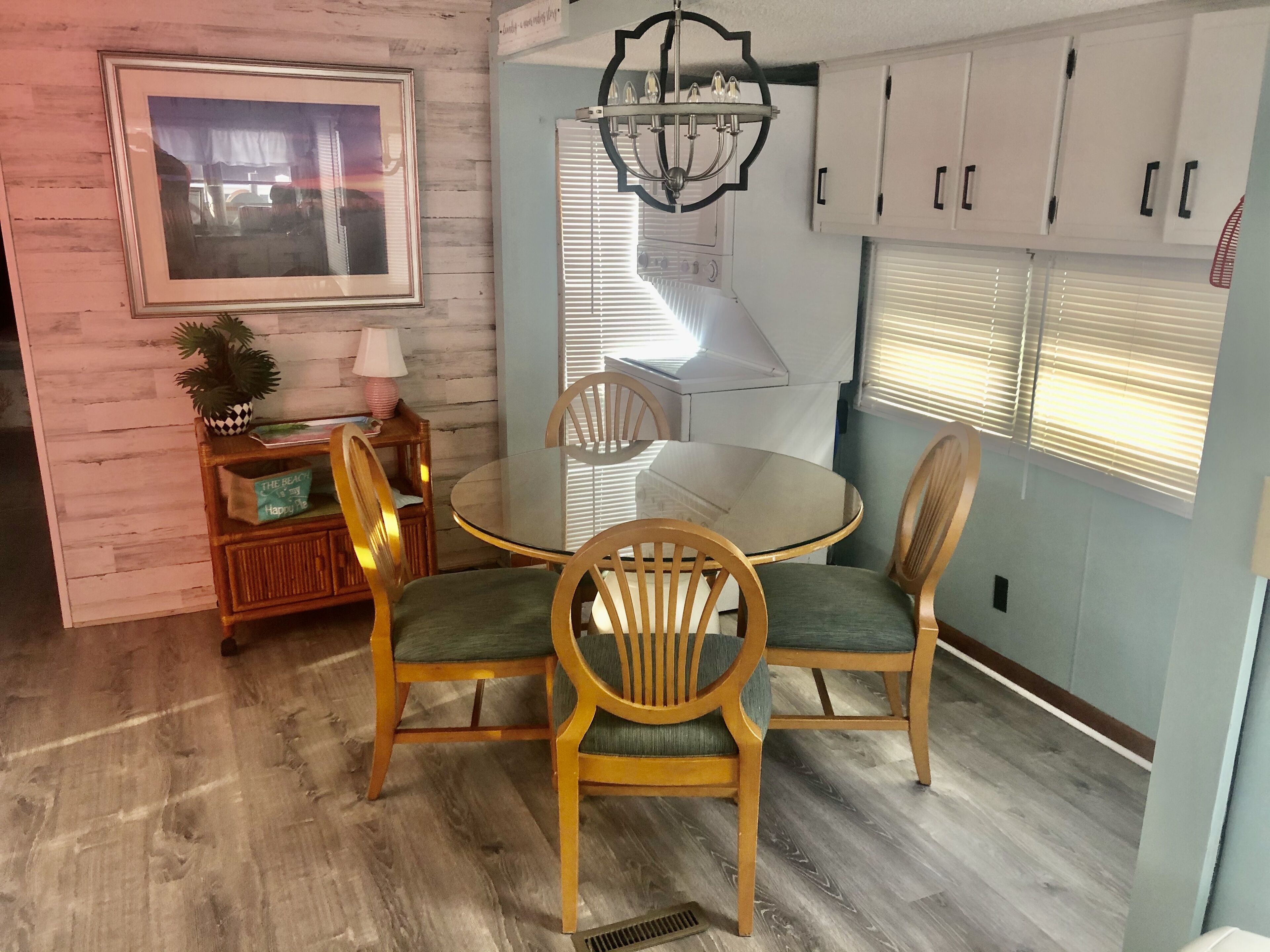 A dining area with a round glass table, wooden chairs, a chandelier, and a framed picture on the wall.