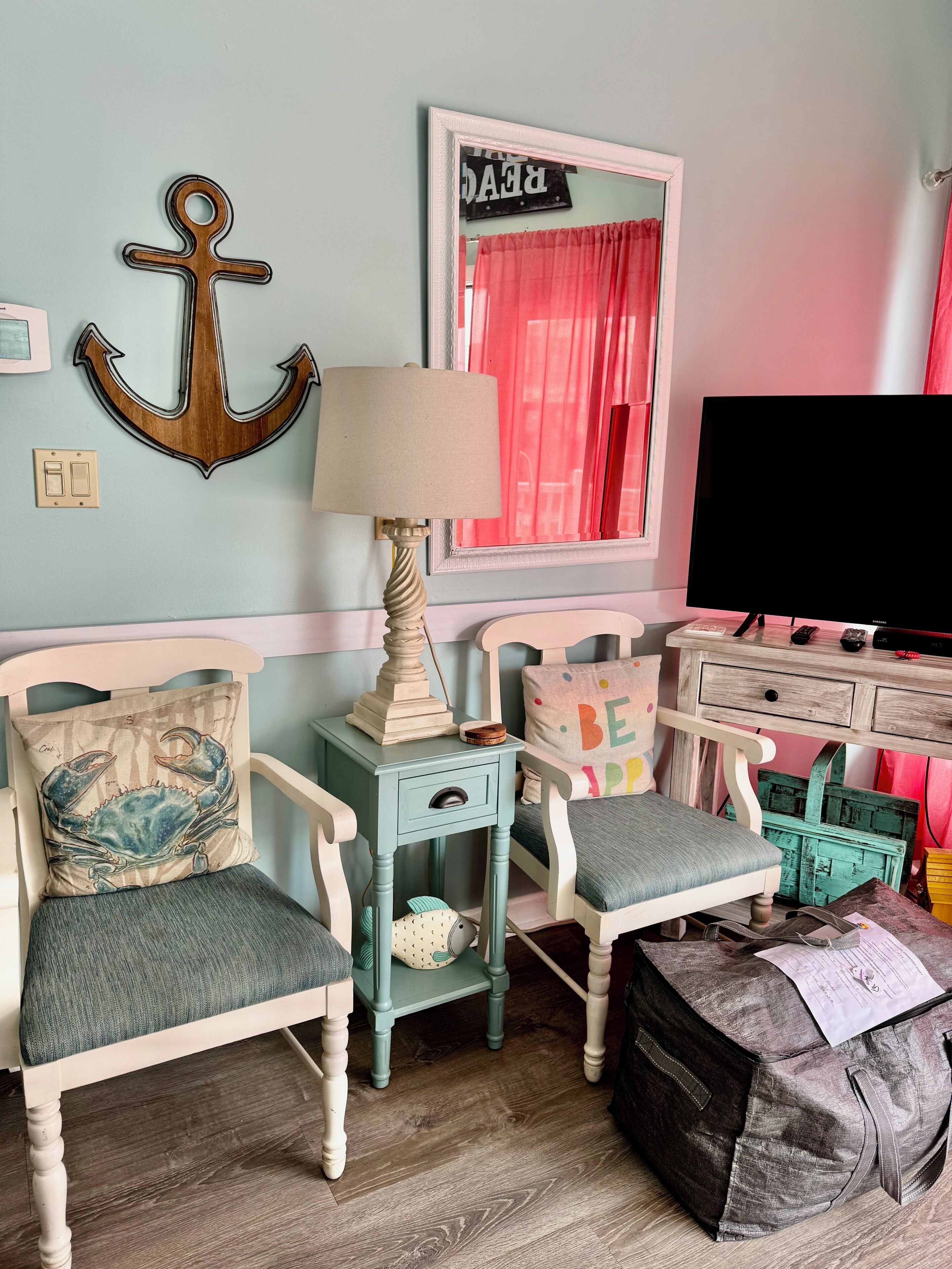 Een kamer met een groenblauwe wand, een houten ankerdecoratie, een lamp, een televisie en een bureau met lades.