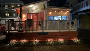A small, brightly lit building with a porch, a welcome sign, and a number sign. - CLOSE TO THE OCEAN ocean lakes site 1048 golf cart Pet friendly (Myrtle Beach)