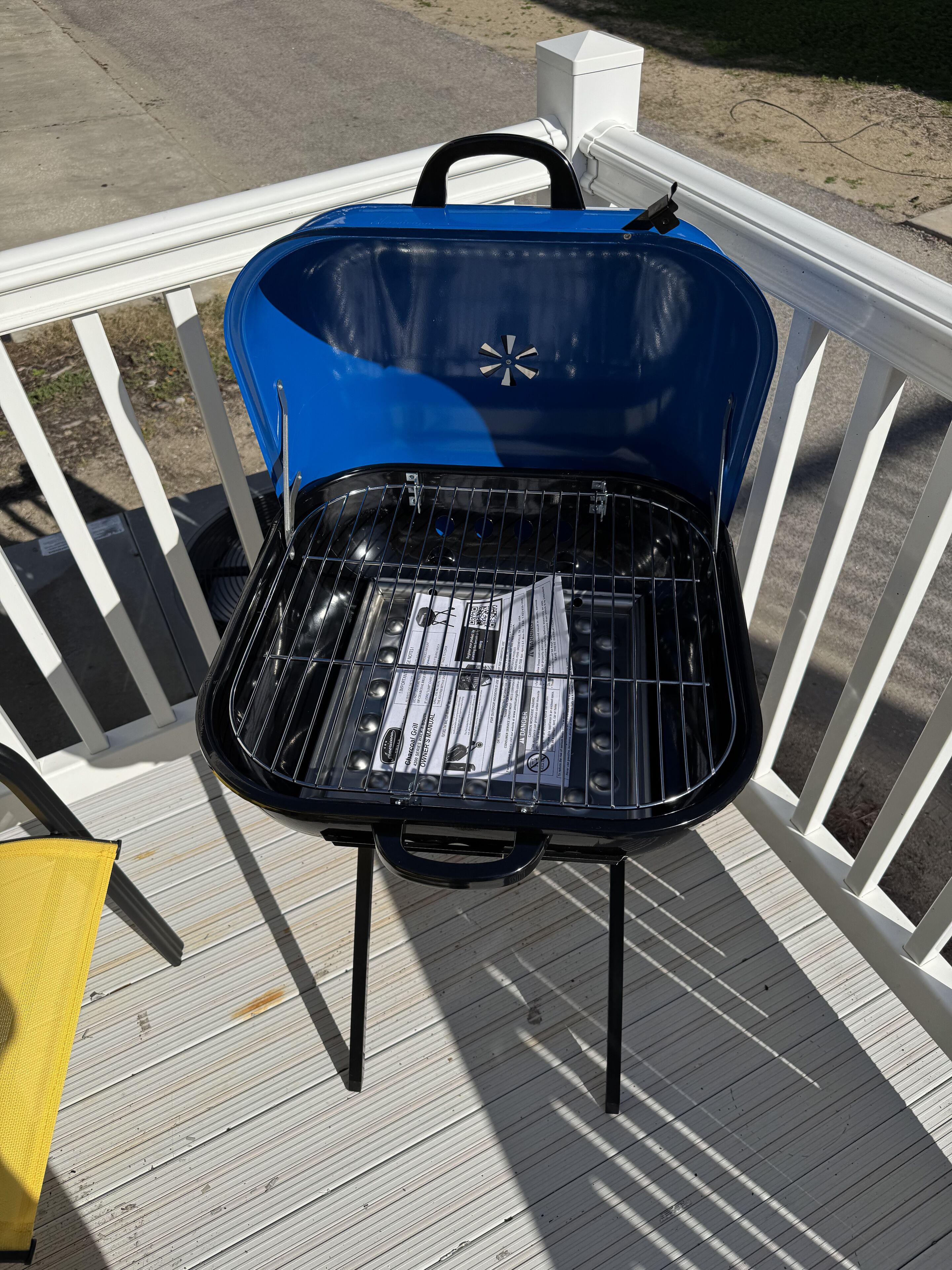 A blue barbecue grill with a black grate, placed on a wooden deck with white railings.