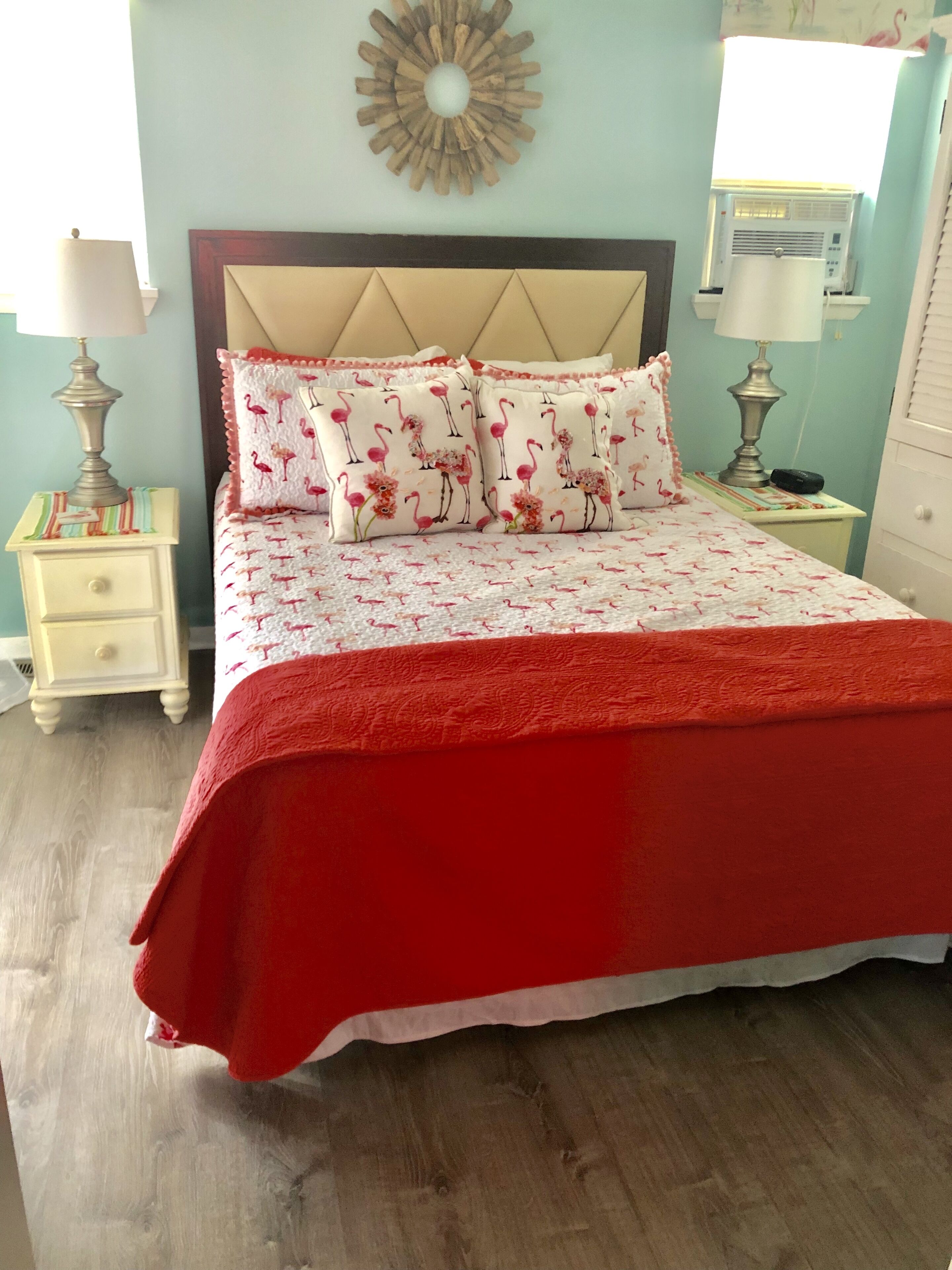 A bedroom with a bed, two nightstands, a wall clock, and a decorative wall piece.