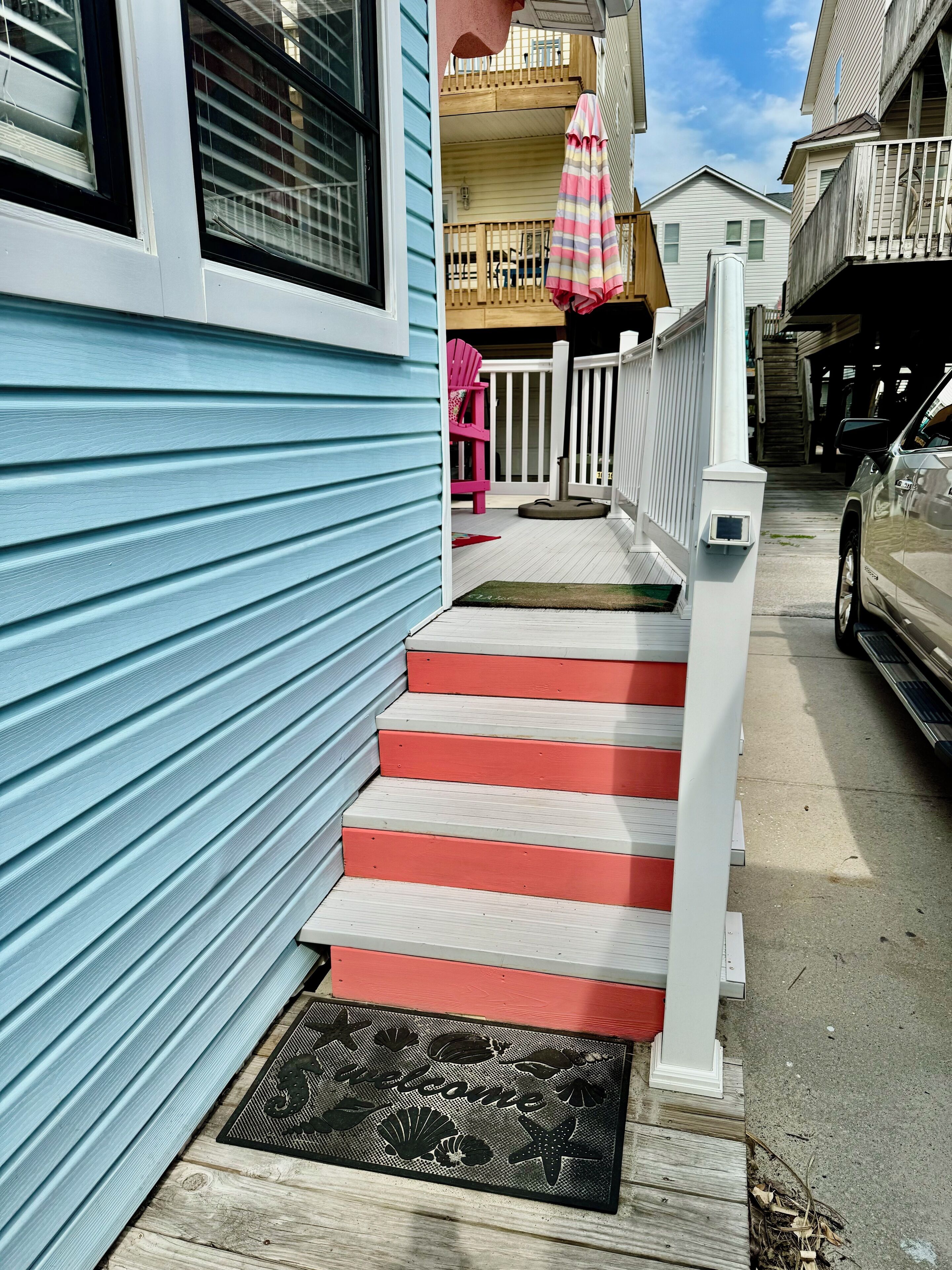 A residential house with a blue exterior, a red and white staircase, a pink chair, and a wooden deck with a white railing.