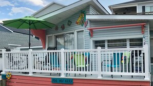 A house with a red lower section and a white upper section, featuring a porch with colorful chairs and a green umbrella. - CLOSE TO THE OCEAN ocean lakes site 1048 golf cart Pet friendly (Myrtle Beach)