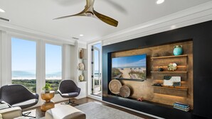 Una sala de estar moderna con un televisor grande, estanterías de madera y un ventilador de techo.