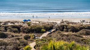 Una playa con un paseo marítimo de madera, sombrillas de playa y algunas personas.