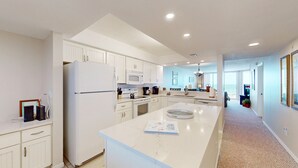 A modern kitchen with white cabinetry, a central island, and a view to the living area.