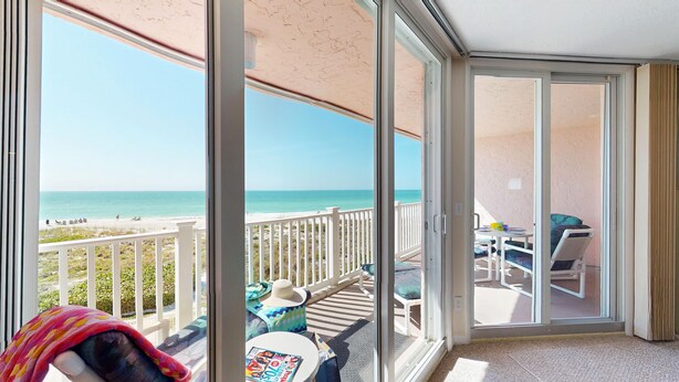 A balcony with a view of the beach, a table with a magazine, and a chair.