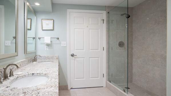 A bathroom with a double sink, a large mirror, a glass shower enclosure, and a white door.