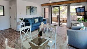 Ein modernes Wohnzimmer mit einem blauen Sofa, einem Glastisch und einem Fernseher im Hintergrund.