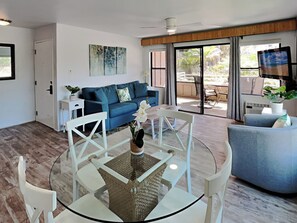 A modern living room with a blue sofa, a glass coffee table, and a TV in the background.