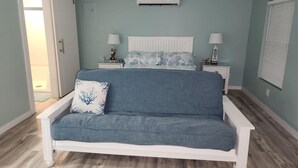 Un dormitorio con una cama blanca, un sofá azul, un ventilador de techo y una ventana con persianas.