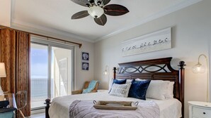 A bedroom with a large bed, a ceiling fan, a view of the balcony, and a nightstand with a lamp.